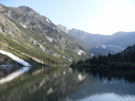 Image of Bertha Lake in Waterton National Park with reflective mirror-like surface reflecting the Rocky Mountains with glaciers and a pine forest under a blue sky